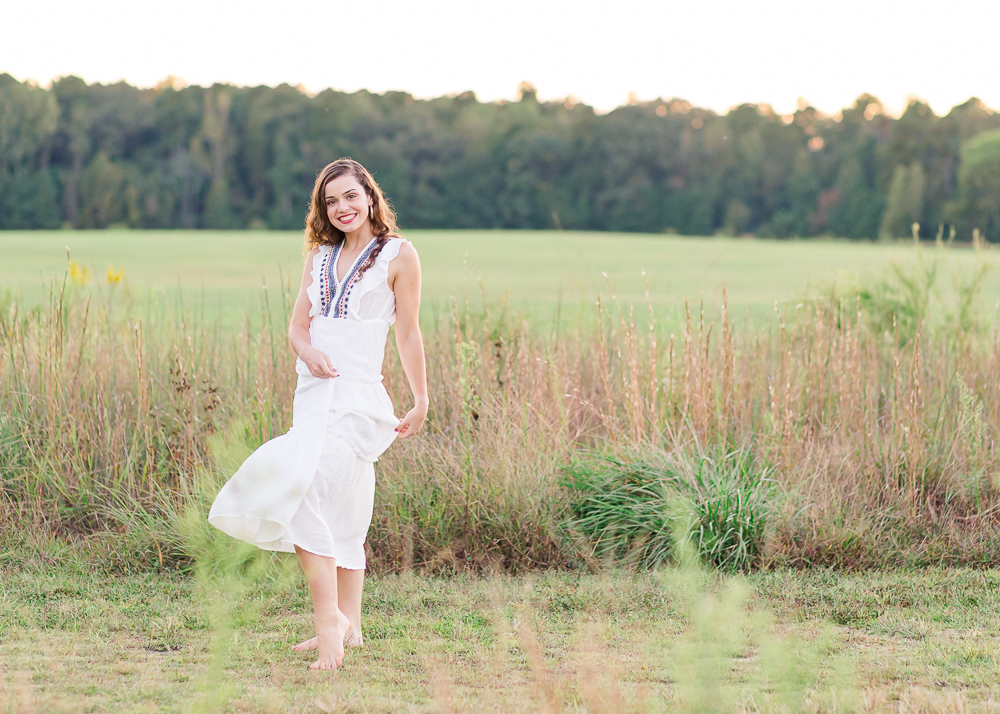 Senior girl portrait session during golden hour at a wheat field wearing a long flowy white dress.