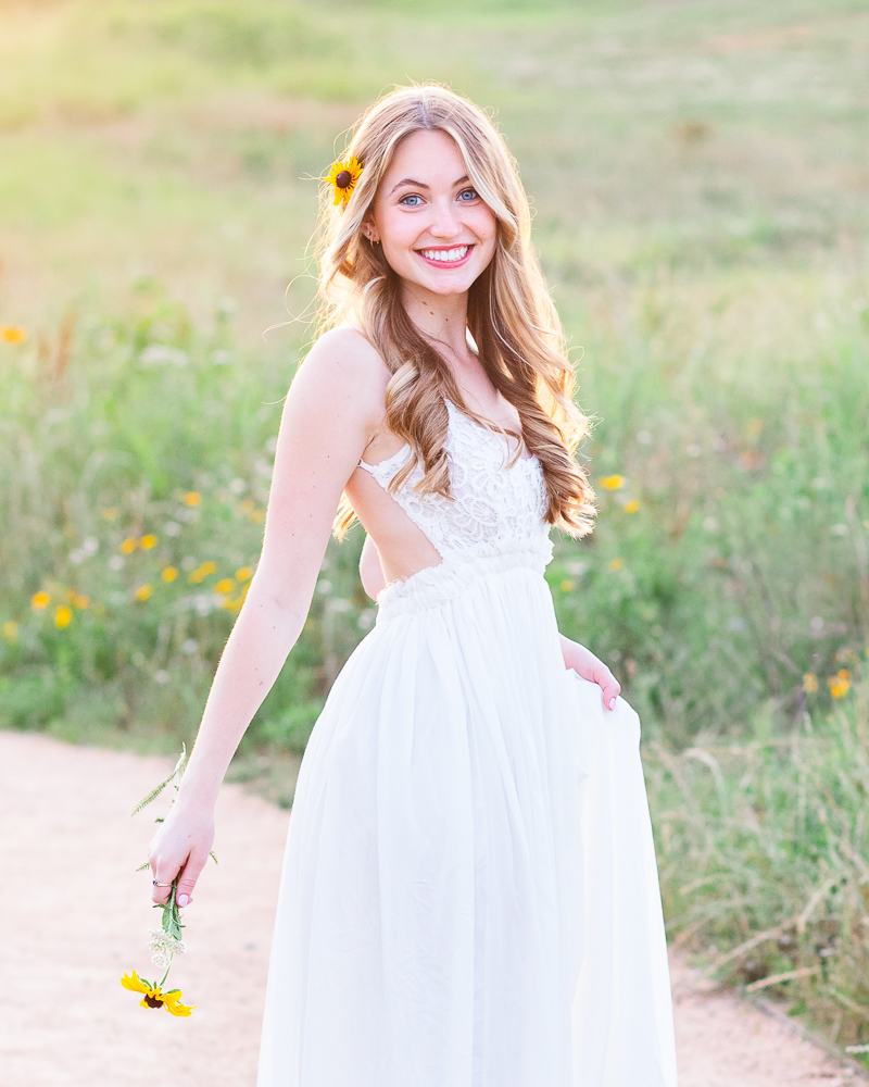 Senior girl in white flowy dress in a field during golden hour session.