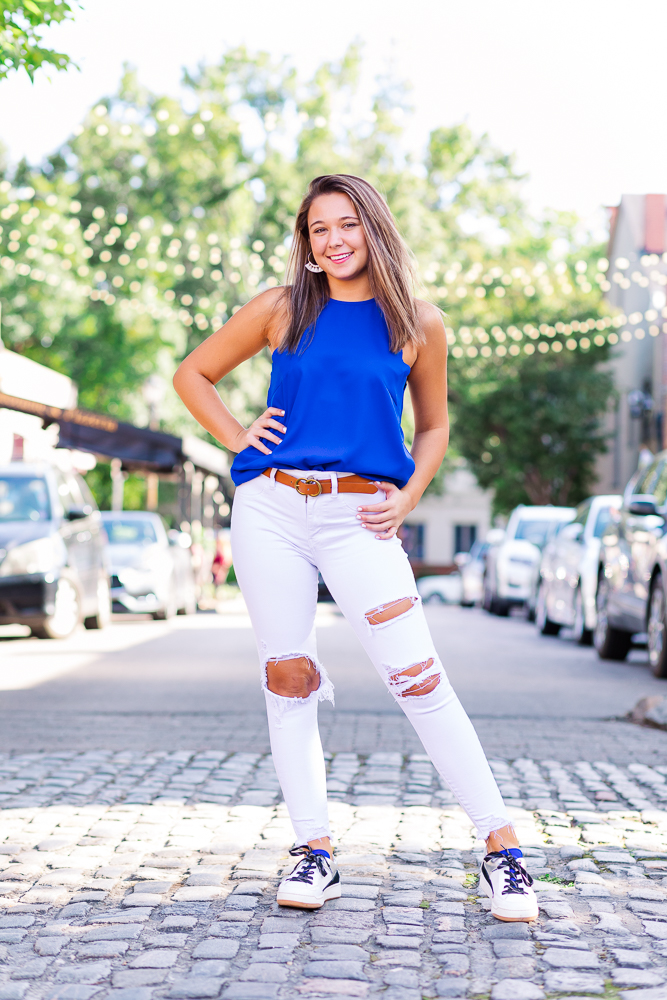 High School Senior Girl with blue shirt and white jeans standing on a cobble stone street in downtown Raleigh, NC.